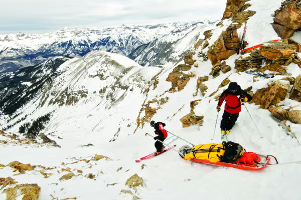 Ski patrol hauling a rescue sled down a steep rocky slope